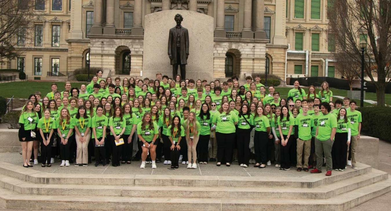Large group of Students in green Youth Day 2024 shirts posing by statue of Abe Lincoln