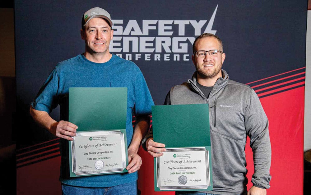 Two smiling men hold award certificates while standing in front of a Safety Energy Conference backdrop